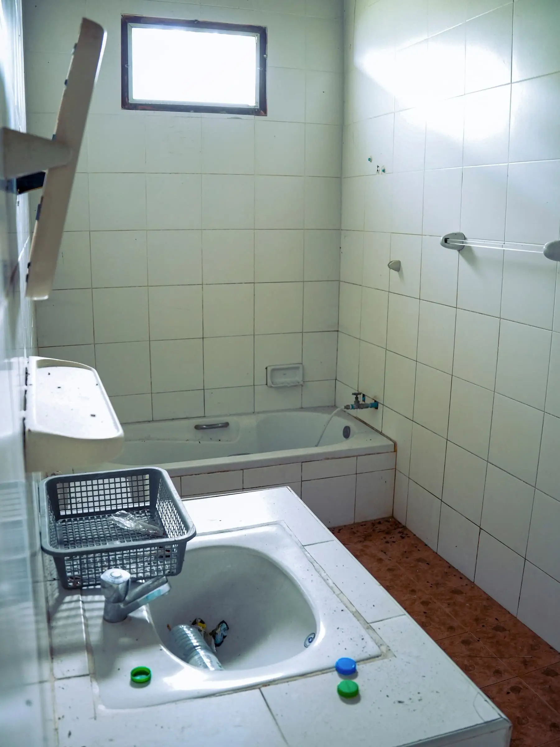 Oude badkamer met vergeelde tegels, bad en wastafel met losse spullen