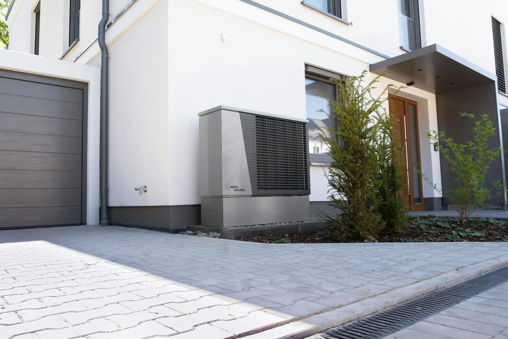 Moderne witte woning met een warmtepomp-buitenunit naast de oprit