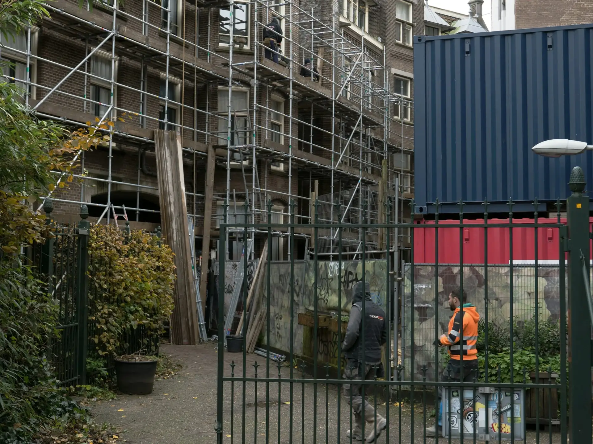 Stelling tegen een gebouw, met werfcontainer en werfhek