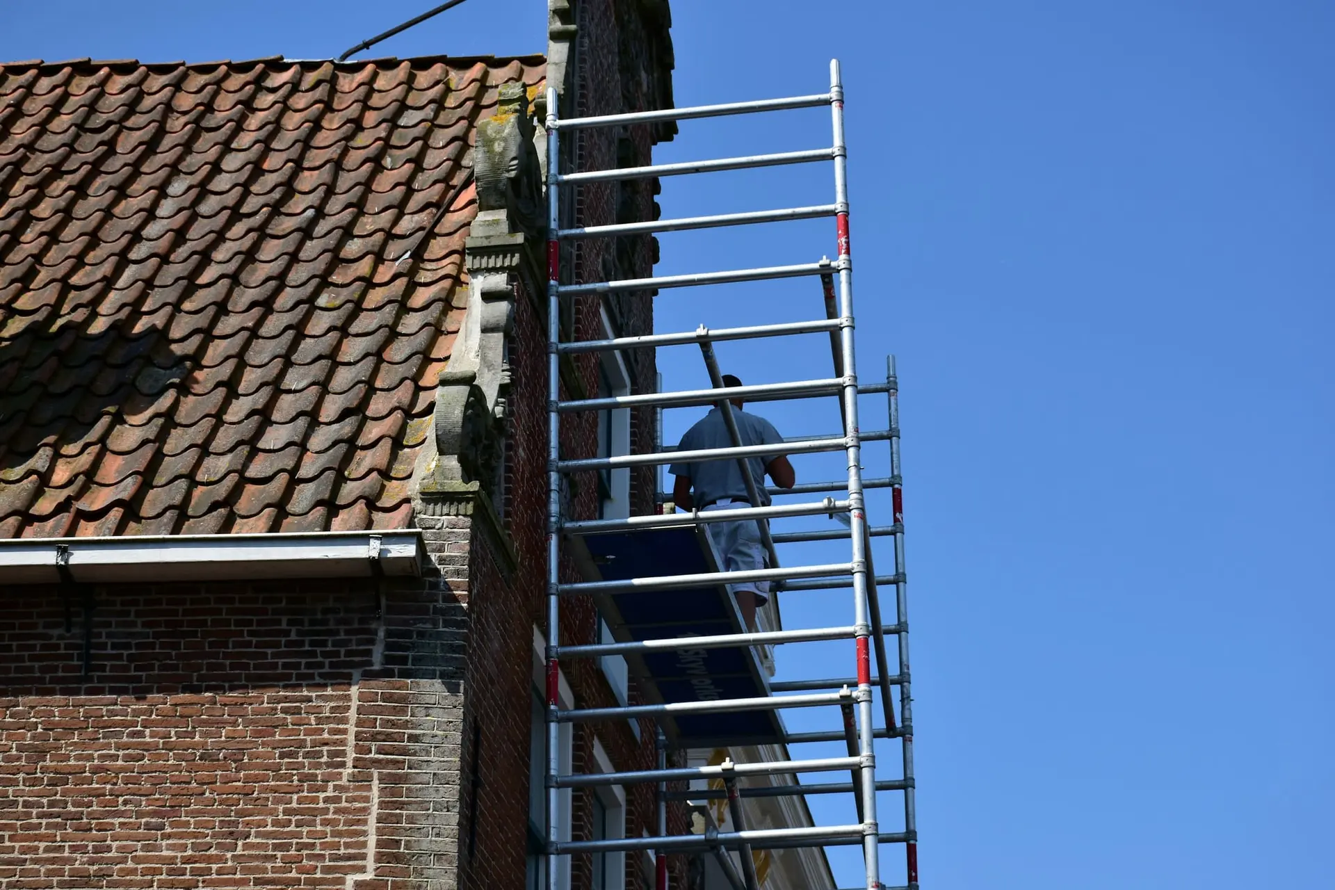 Baksteengevel en pannendak met een smalle stelling tegen een blauwe lucht
