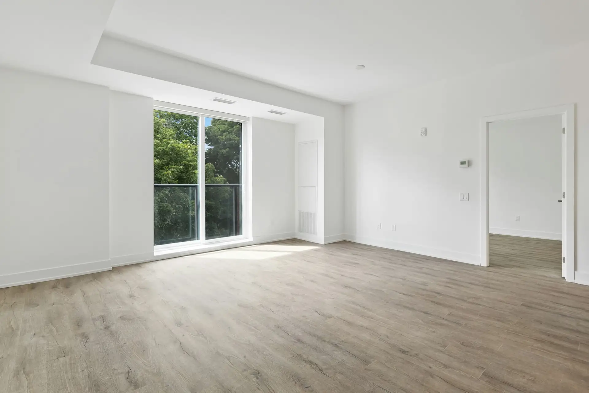 Lege, lichte kamer met nieuwe vloer en brede schuifdeur