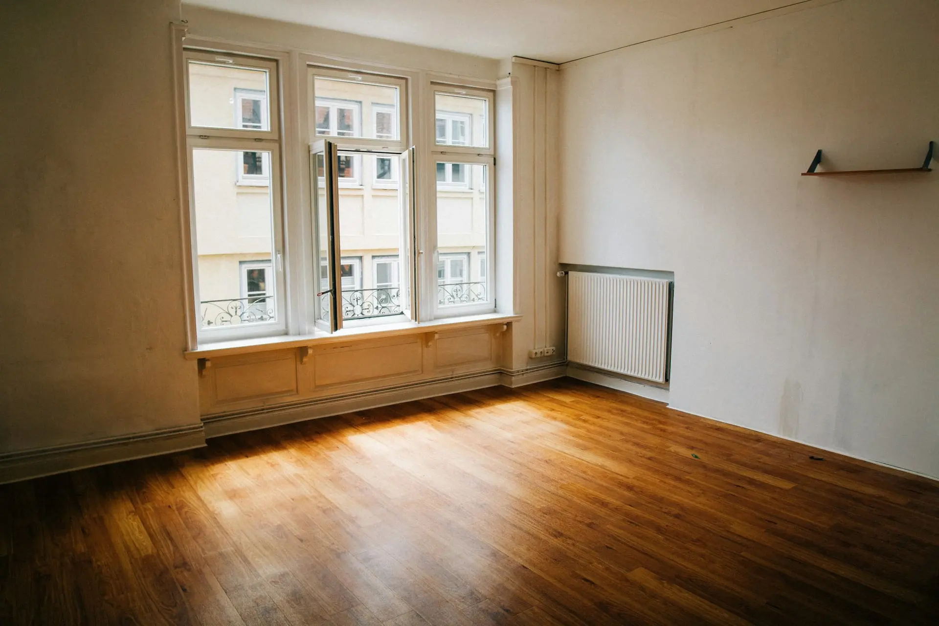 Lege kamer met kale muren, oude radiator en een brede raampartij