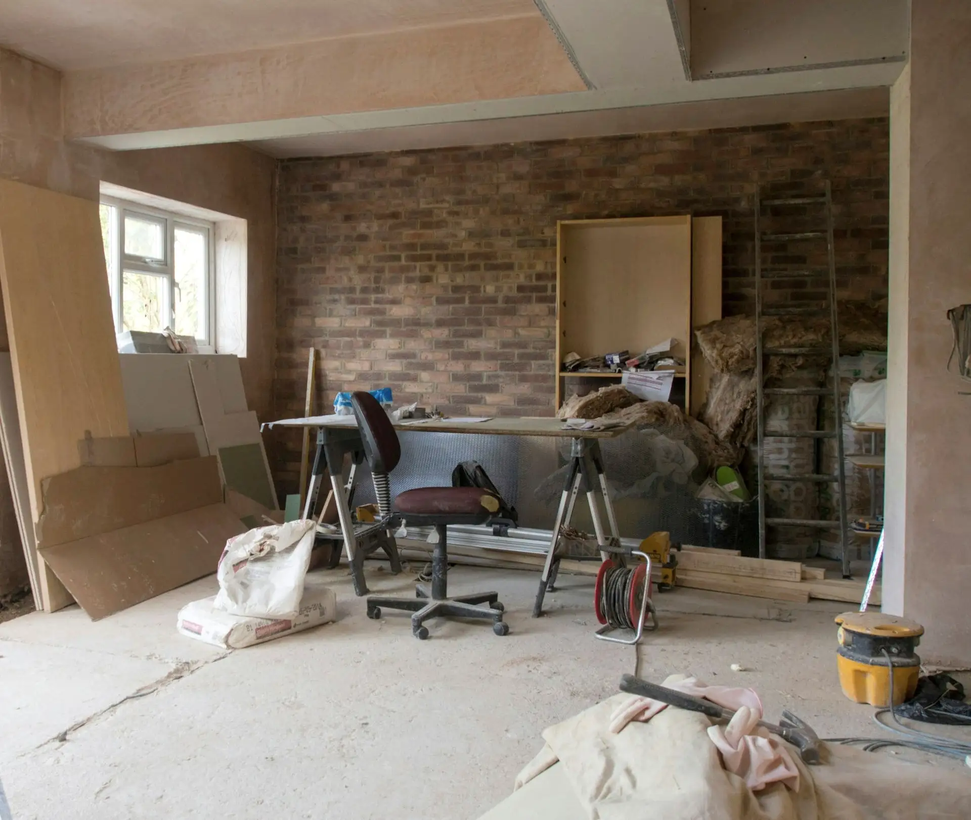 De nieuwe leefruimte tijdens de werf: bakstenen wand, verse pleister, schragen, materiaal en een ladder