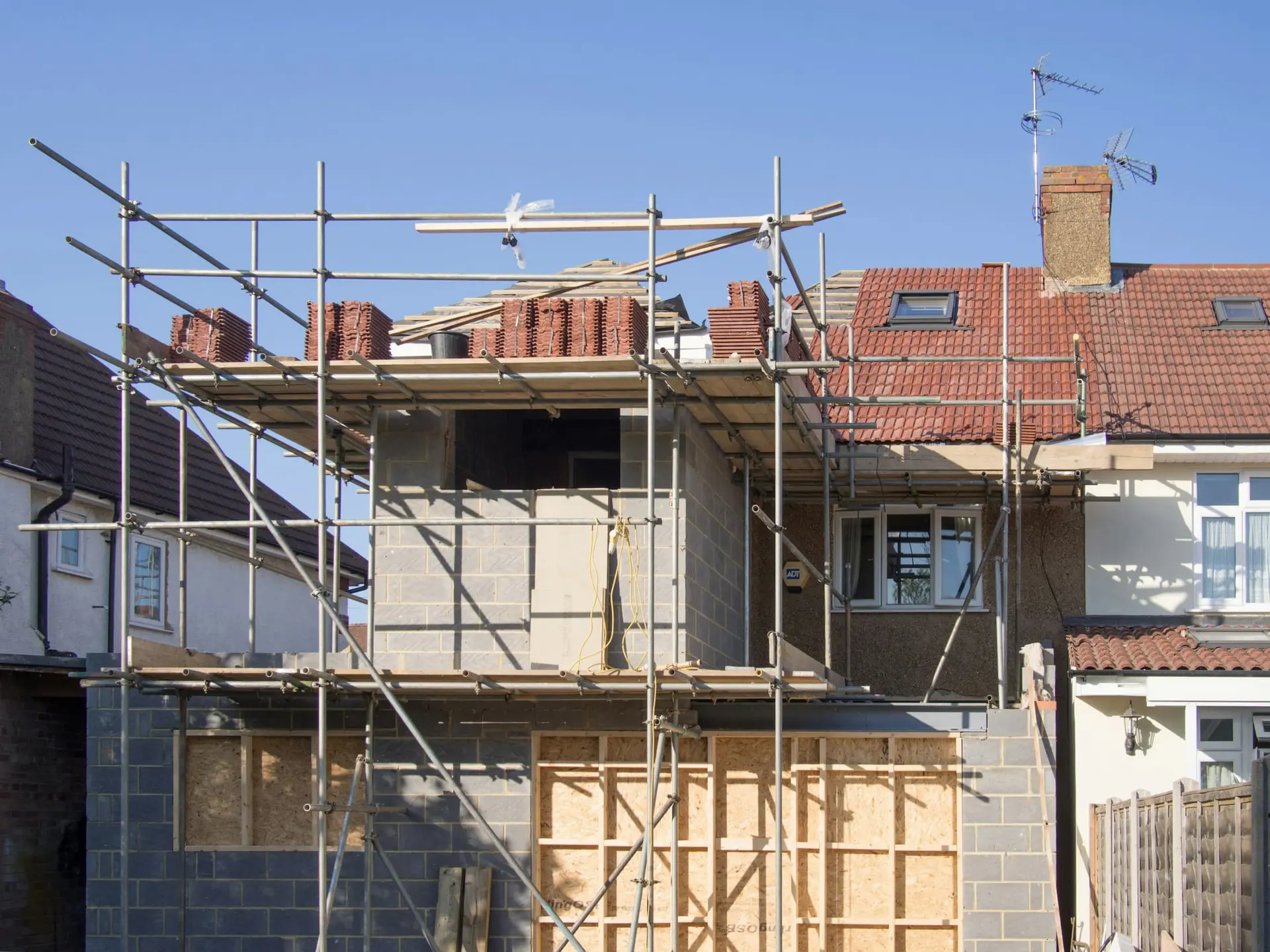 Rijwoning in de stelling tijdens de ruwbouw van een aanbouw met extra verdieping, onder een blauwe lucht