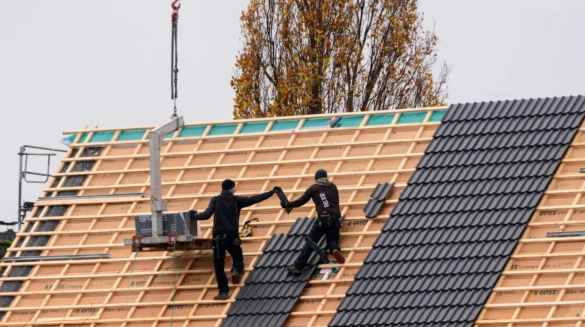 Twee dakwerkers leggen donkere dakpannen op een nieuw onderdak met panlatten