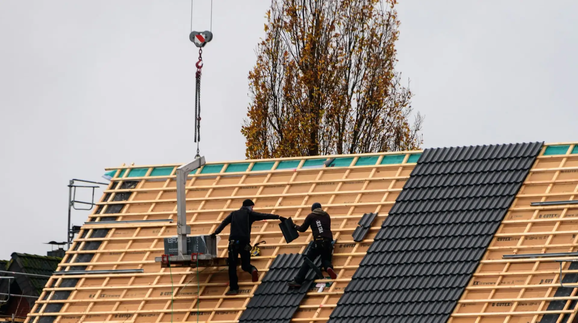 Twee dakwerkers en een kraan boven het open dakvlak