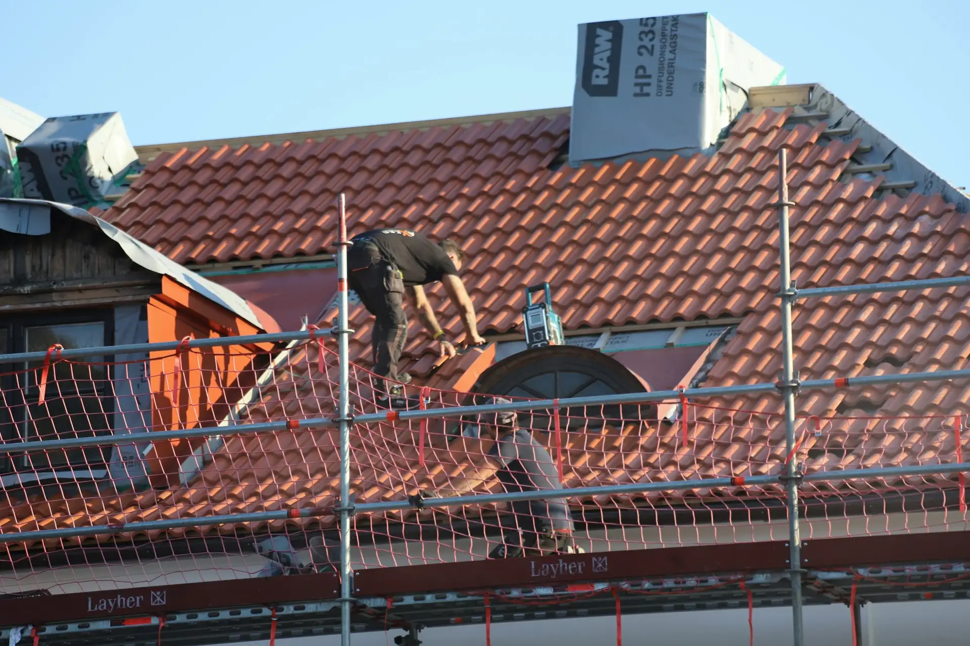 Dakwerker snijdt pannen op een rood dak met valbeveiliging