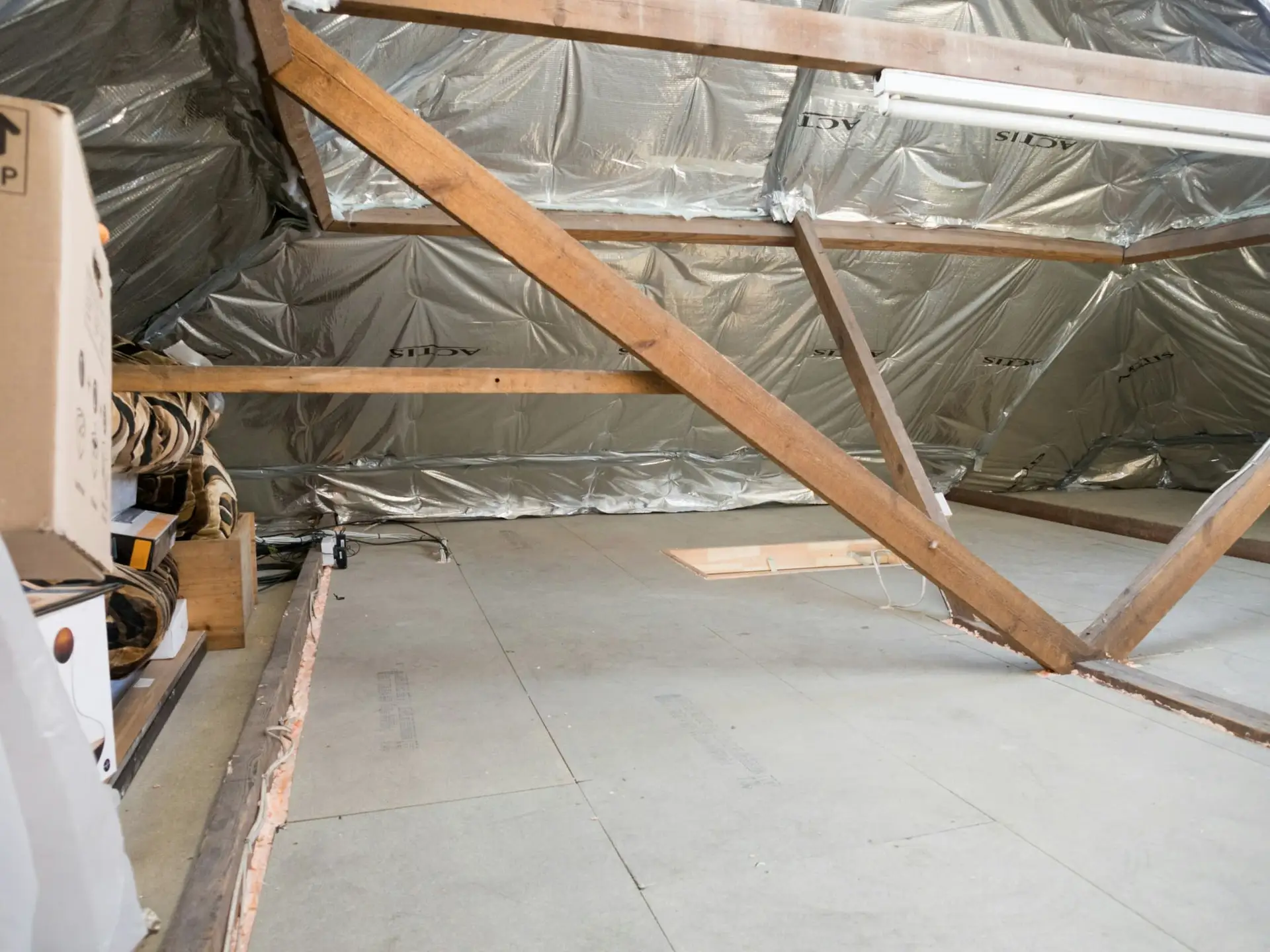 Onafgewerkte zolder met isolatiefolie, houten spanten en een ruwe vloer
