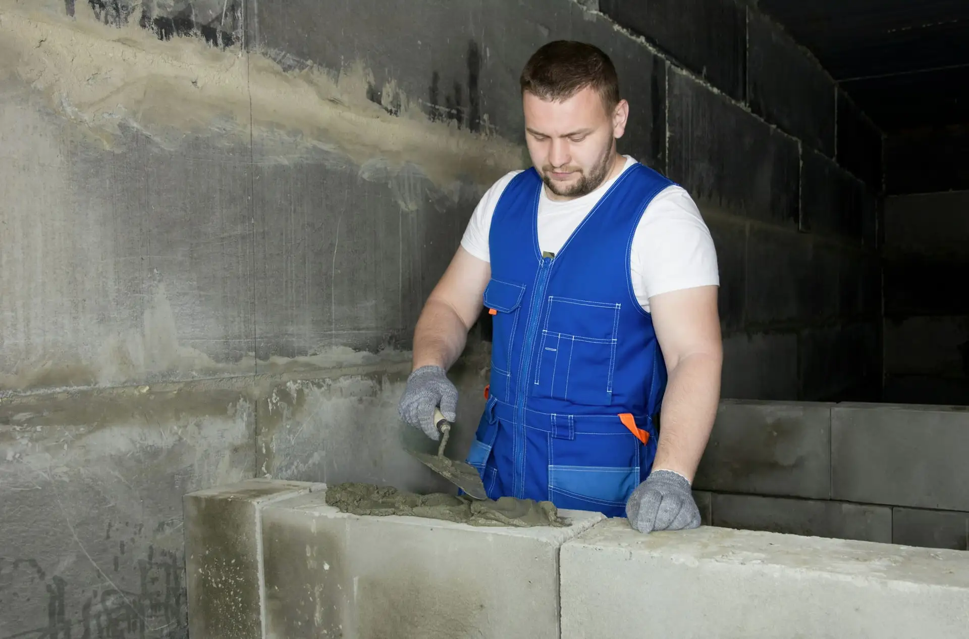 Metser in blauwe overall werkt aan een blokkenmuur