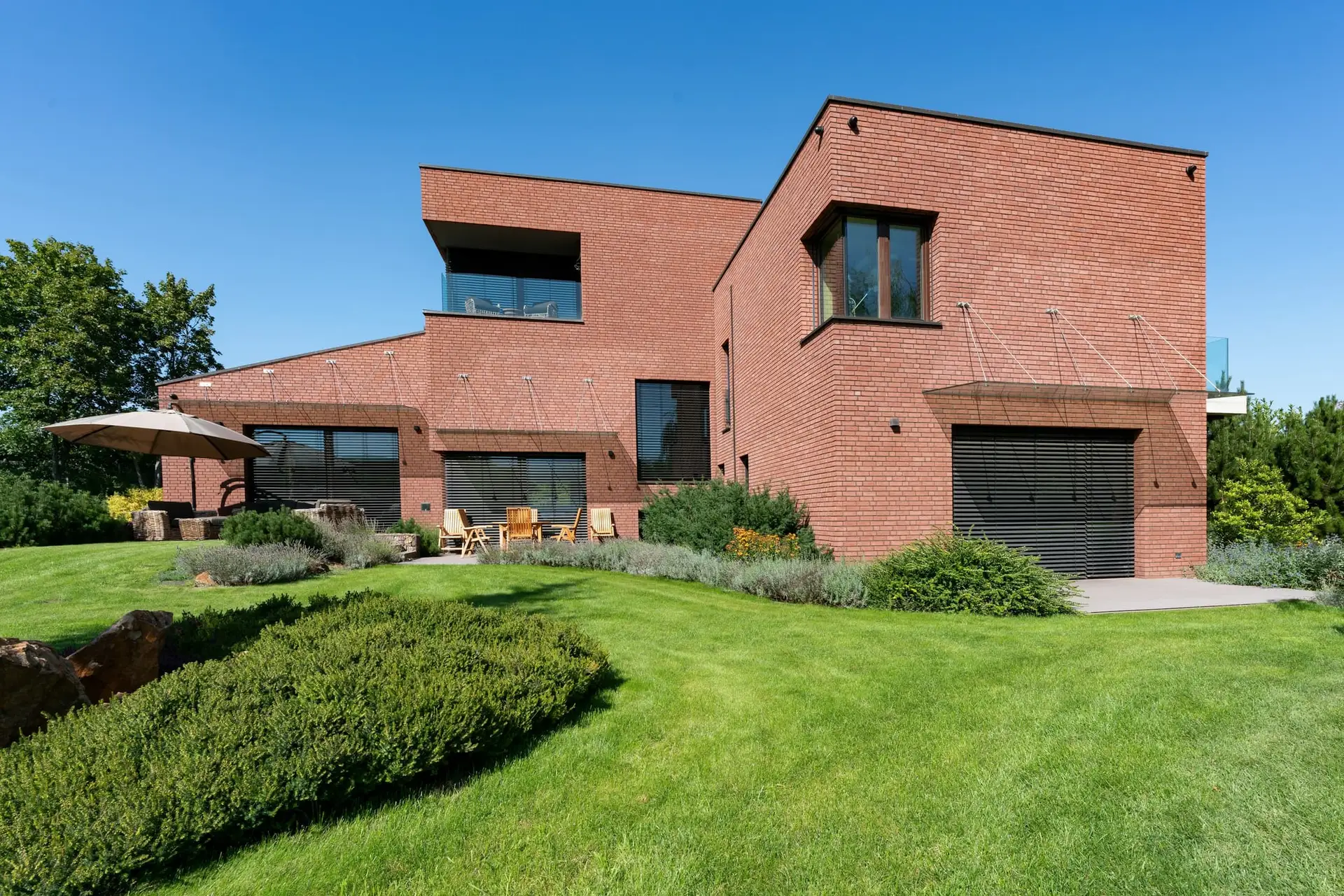 Moderne woning in rode baksteen met een grote groene tuin onder een blauwe lucht